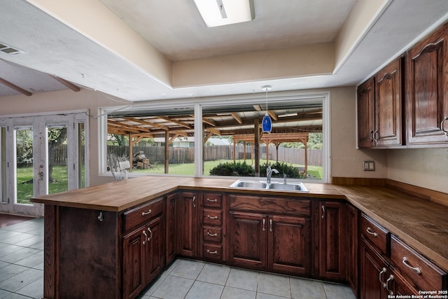 6914 Glen Gate, San Antonio, TX 78239 - kitchen with light tile patterned floors, wooden counters, a peninsula, and dark brown cabinetry