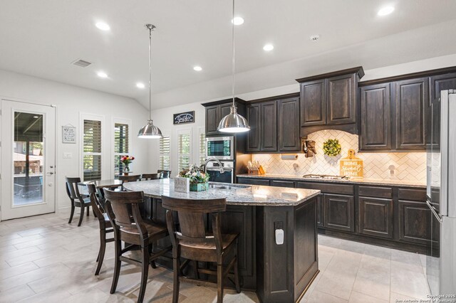 130 Boulder Crk, Boerne, TX 78006 - kitchen with appliances with stainless steel finishes, an island with sink, a kitchen breakfast bar, light stone counters, and tasteful backsplash