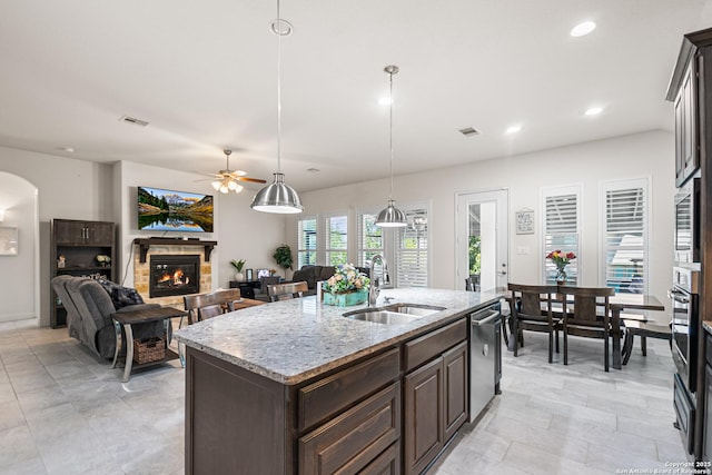 130 Boulder Crk, Boerne, TX 78006 - kitchen with appliances with stainless steel finishes, dark brown cabinets, ceiling fan, a fireplace, and a center island with sink