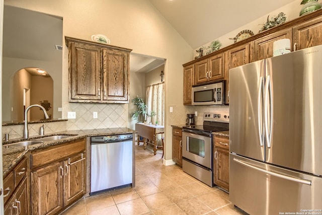 1463 Birch Ln, Fischer, TX 78623 - kitchen featuring appliances with stainless steel finishes, dark stone counters, decorative backsplash, light tile patterned floors, and high vaulted ceiling