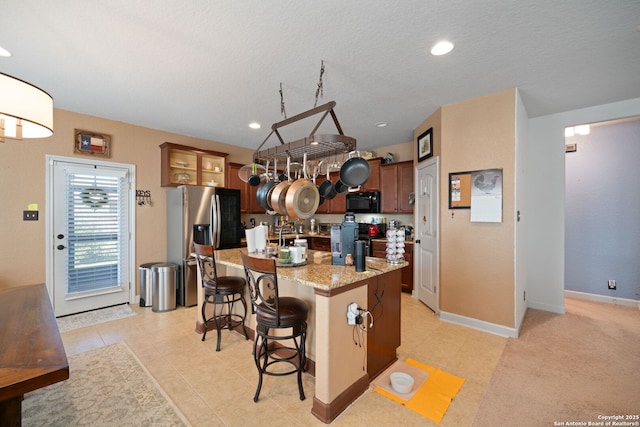 1573 Las Fontanasa, New Braunfels, TX 78132 - kitchen with black microwave, stainless steel fridge, a center island with sink, a kitchen breakfast bar, and range