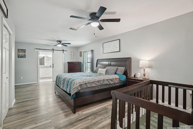 714 N Esplanade, Karnes City, TX 78118 - bedroom with a barn door, wood finished floors, connected bathroom, and ceiling fan