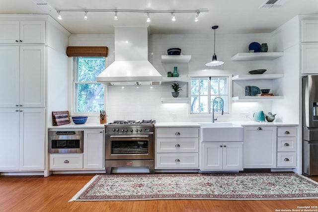 158 Laurel Hts, San Antonio, TX 78212 - kitchen featuring open shelves, stainless steel appliances, wall chimney range hood, rail lighting, and light wood-type flooring
