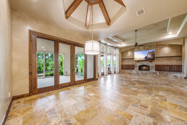 1437 Decanter, New Braunfels, TX 78132 - unfurnished living room featuring a ceiling fan, stone tile flooring, a tray ceiling, built in shelves, and a fireplace