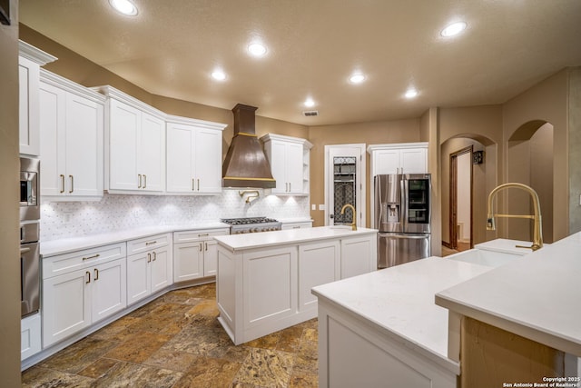 1437 Decanter, New Braunfels, TX 78132 - kitchen featuring appliances with stainless steel finishes, premium range hood, a center island with sink, stone tile flooring, and tasteful backsplash