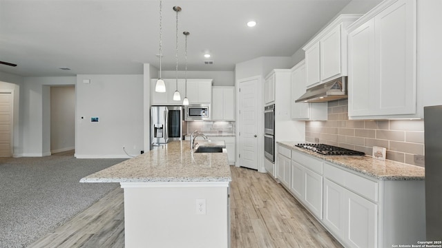 1606 Folk Victorian, New Braunfels, TX 78132 - kitchen with stainless steel appliances, under cabinet range hood, white cabinetry, decorative backsplash, and a kitchen island with sink