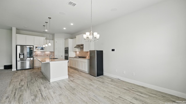 1606 Folk Victorian, New Braunfels, TX 78132 - kitchen with appliances with stainless steel finishes, a chandelier, under cabinet range hood, decorative backsplash, and light wood finished floors