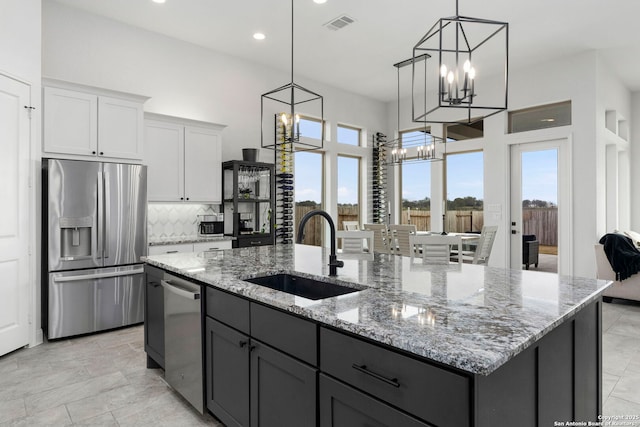 2905 Harvest Moon, Seguin, TX 78155 - kitchen featuring appliances with stainless steel finishes, a chandelier, a kitchen island with sink, backsplash, and light stone counters