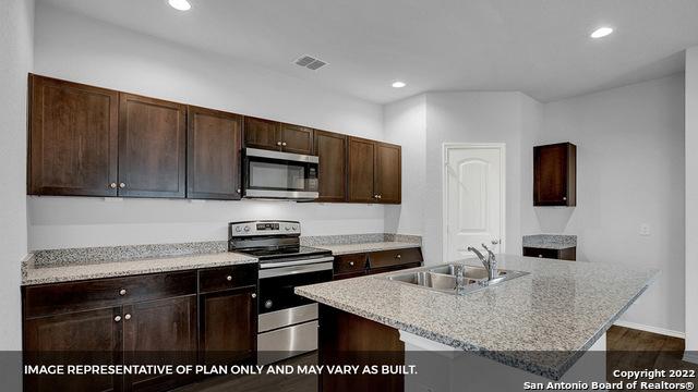 21039 Watercourse Way, San Antonio, TX 78266 - kitchen featuring appliances with stainless steel finishes, dark brown cabinetry, recessed lighting, a center island with sink, and light stone countertops