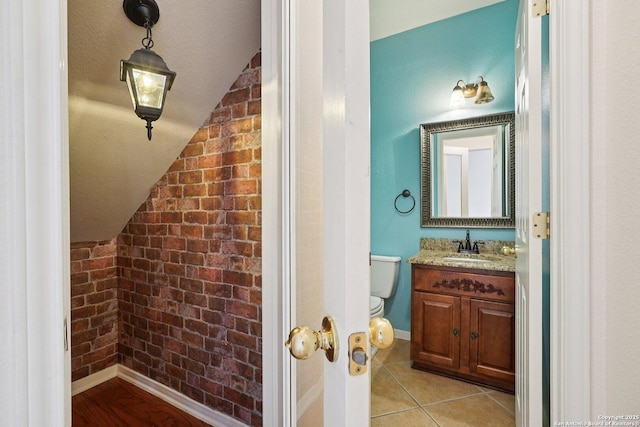 519 Catanbo, San Antonio, TX 78258 - half bath with vaulted ceiling, vanity, tile patterned flooring, and brick wall