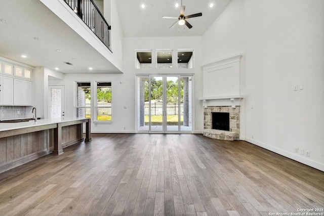 228 Dulce Vis, Boerne, TX 78006 - unfurnished living room with a towering ceiling, a ceiling fan, wood finished floors, a stone fireplace, and recessed lighting