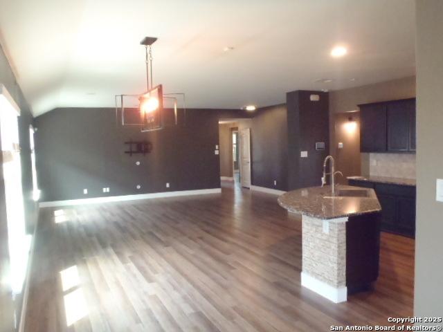 2690 Mccrae, New Braunfels, TX 78130 - kitchen with wood finished floors, a center island with sink, tasteful backsplash, stone countertops, and lofted ceiling