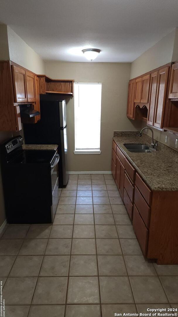 1826 Laven Dr, San Antonio, TX 78228 - kitchen featuring appliances with stainless steel finishes, under cabinet range hood, light tile patterned flooring, brown cabinetry, and stone countertops