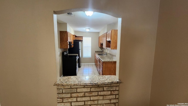 1826 Laven Dr, San Antonio, TX 78228 - kitchen with black range with electric stovetop, brown cabinets, light tile patterned floors, and arched walkways