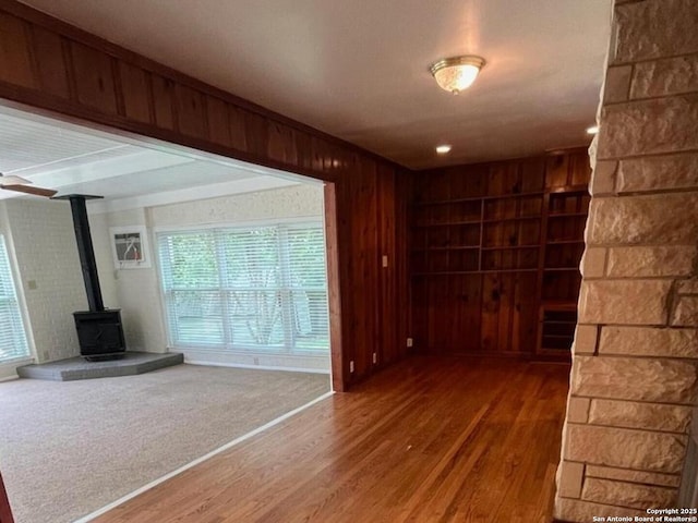 117 Bryker, Terrell Hills, TX 78209 - unfurnished living room with wood finished floors, a wood stove, healthy amount of natural light, and wood walls