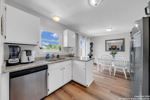 808 Fern Mdw, Universal City, TX 78148 - kitchen with stainless steel appliances, light wood-style flooring, white cabinets, light stone counters, and a peninsula