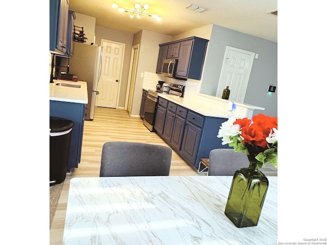 5742 Butch Cyn, San Antonio, TX 78252 - kitchen featuring appliances with stainless steel finishes, decorative backsplash, light countertops, light wood finished floors, and a chandelier