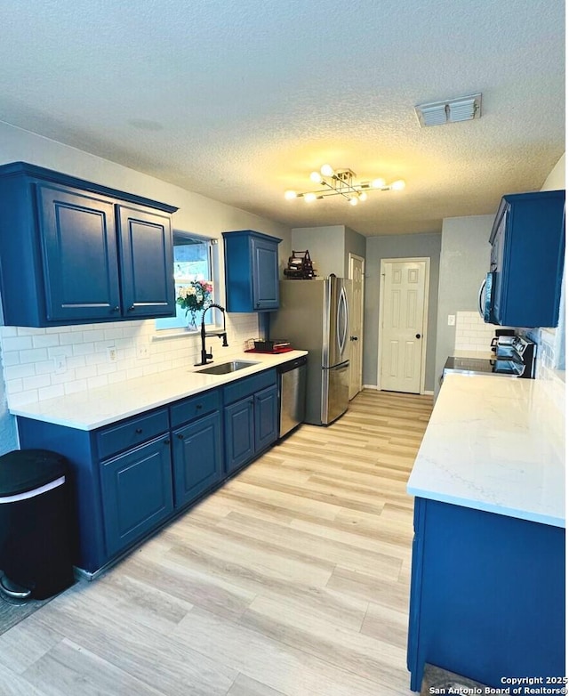 5742 Butch Cyn, San Antonio, TX 78252 - kitchen featuring blue cabinets, appliances with stainless steel finishes, light countertops, decorative backsplash, and light wood-style flooring