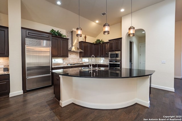 12 Denbury Gln, San Antonio, TX 78257 - kitchen featuring built in appliances, wall chimney exhaust hood, arched walkways, tasteful backsplash, and dark brown cabinetry