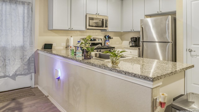 7207 Rosada Way, San Antonio, TX 78218 - kitchen featuring appliances with stainless steel finishes, a peninsula, wood finished floors, and light stone countertops
