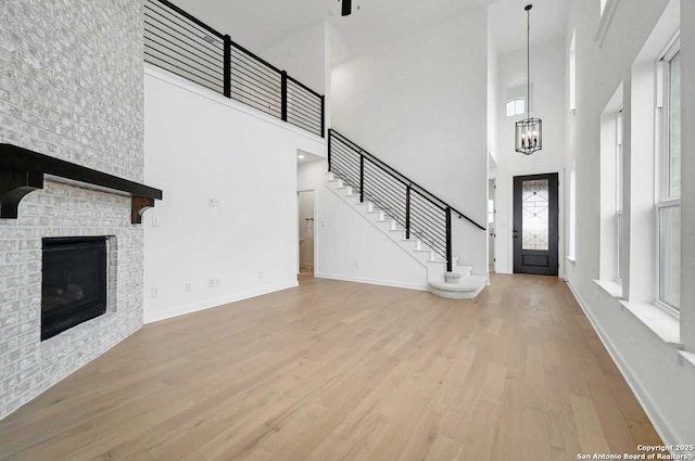 233 Alpine, New Braunfels, TX 78130 - unfurnished living room featuring a high ceiling, wood finished floors, a chandelier, a brick fireplace, and stairs