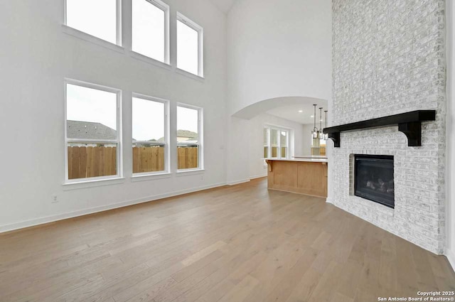 233 Alpine, New Braunfels, TX 78130 - unfurnished living room with light wood-style flooring, arched walkways, a towering ceiling, plenty of natural light, and a fireplace