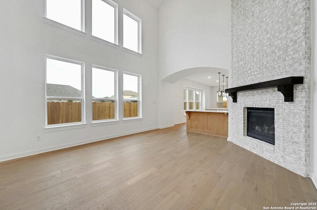 233 Alpine, New Braunfels, TX 78130 - unfurnished living room with light wood-type flooring, a towering ceiling, arched walkways, healthy amount of natural light, and a brick fireplace