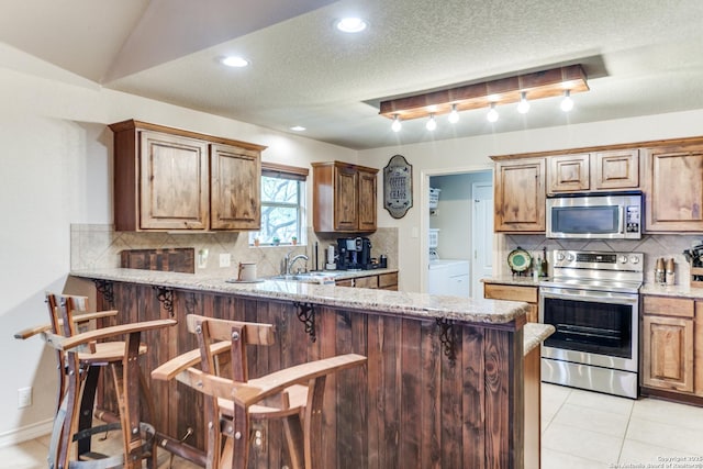 1777 Crossbow, Canyon Lake, TX 78133 - kitchen featuring appliances with stainless steel finishes, light tile patterned flooring, decorative backsplash, a kitchen breakfast bar, and a textured ceiling