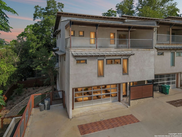 305 Joliet Unit D, San Antonio, TX 78209 - back of property at dusk featuring stucco siding, an attached garage, concrete driveway, a balcony, and a standing seam roof