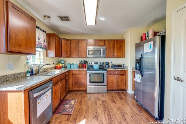 812 Riviere, Falls City, TX 78113 - kitchen featuring appliances with stainless steel finishes, brown cabinetry, wood finished floors, and light stone countertops