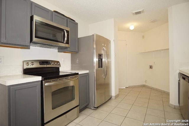 5615 Camry Spgs, San Antonio, TX 78251 - kitchen featuring stainless steel appliances, gray cabinetry, light tile patterned flooring, and tile counters