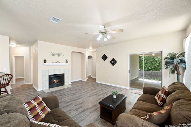 1905 Walter Raleigh, Windcrest, TX 78239 - living room featuring arched walkways, a ceiling fan, wood finished floors, a textured ceiling, and a tiled fireplace