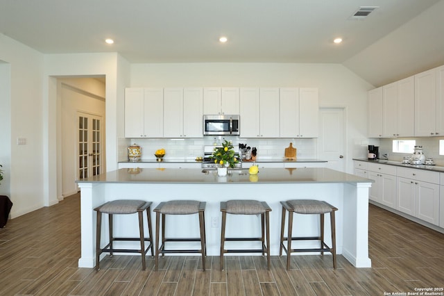 5798 Luciano Trl, Seguin, TX 78155 - kitchen with stainless steel microwave, dark wood-type flooring, decorative backsplash, a breakfast bar area, and lofted ceiling