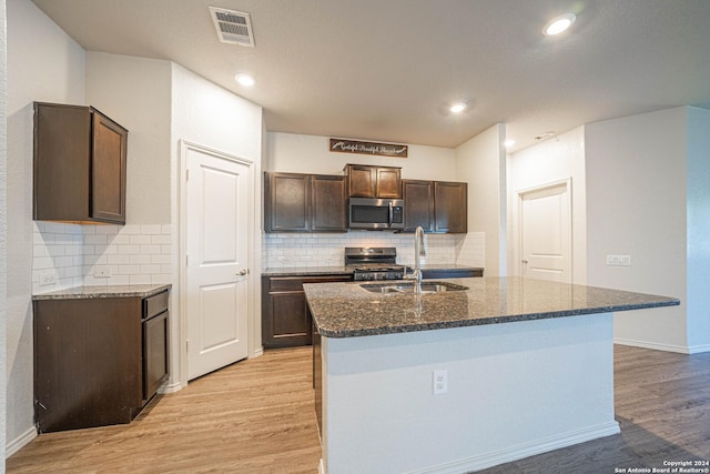 7119 Magnolia Blf, San Antonio, TX 78218 - kitchen with stainless steel appliances, light wood finished floors, dark stone counters, an island with sink, and dark brown cabinets