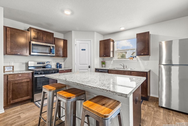 1006 Pacific Monarch, San Antonio, TX 78253 - kitchen with stainless steel appliances, light wood-style flooring, a center island, a breakfast bar, and light stone countertops