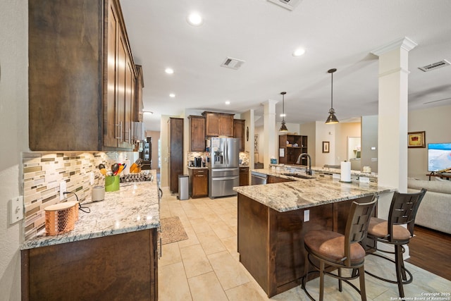 20926 Encino Dawn, San Antonio, TX 78259 - kitchen featuring appliances with stainless steel finishes, decorative columns, a kitchen bar, tasteful backsplash, and light stone countertops