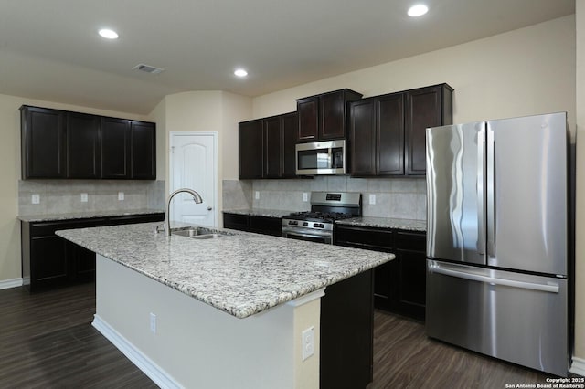 13027 Maestro Spark, San Antonio, TX 78252 - kitchen with appliances with stainless steel finishes, dark wood finished floors, backsplash, a kitchen island with sink, and light stone countertops
