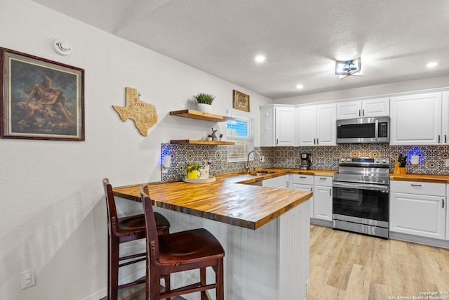 6402 Quiet Frst, San Antonio, TX 78239 - kitchen featuring appliances with stainless steel finishes, butcher block countertops, backsplash, a peninsula, and white cabinetry