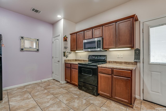 1038 Marquette, San Antonio, TX 78228 - kitchen with stainless steel microwave, black / electric stove, light countertops, brown cabinets, and light tile patterned floors