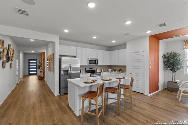 10554 Briceway Clb, San Antonio, TX 78254 - kitchen with stainless steel appliances, light countertops, light wood finished floors, white cabinetry, and a breakfast bar area