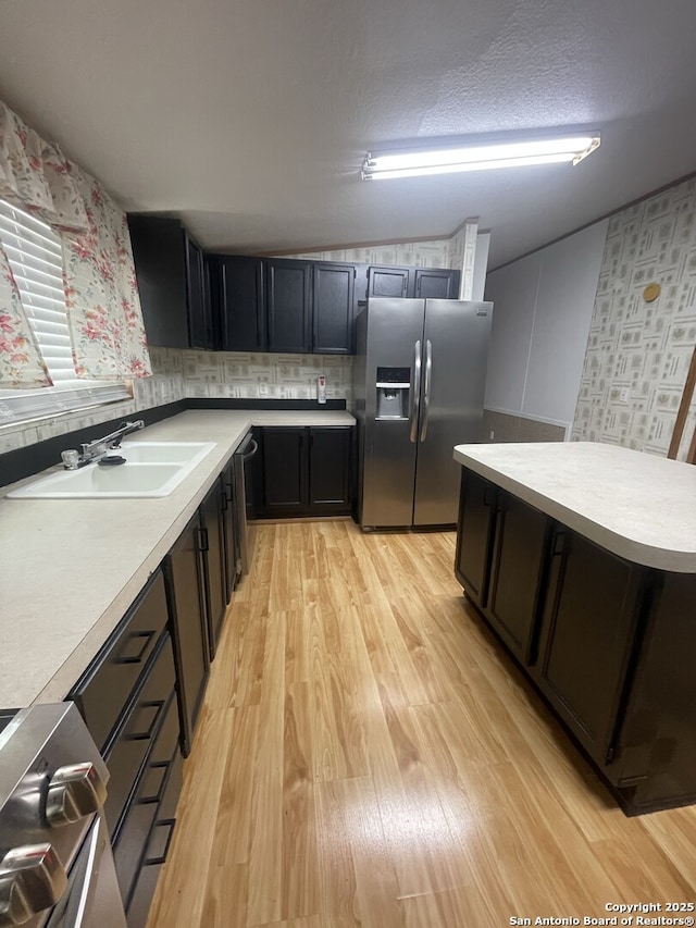 207 S Edwards, Charlotte, TX 78011 - kitchen with appliances with stainless steel finishes, light wood-style flooring, light countertops, wallpapered walls, and dark cabinets