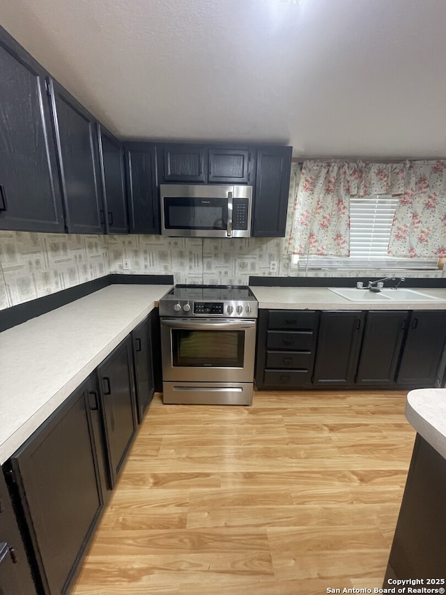 207 S Edwards, Charlotte, TX 78011 - kitchen featuring stainless steel appliances, light countertops, light wood-style floors, wallpapered walls, and dark cabinetry