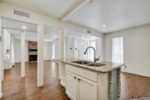 11826 Petal Unit 73, San Antonio, TX 78216 - kitchen with dark wood-style floors, light stone countertops, a center island with sink, recessed lighting, and a brick fireplace
