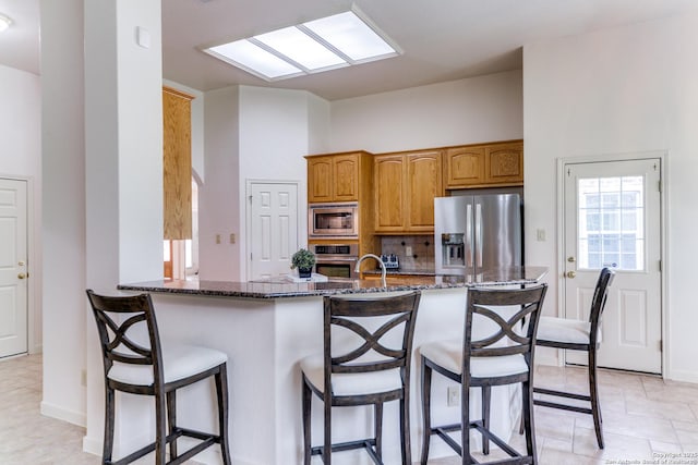 15311 Tamaron Pass, San Antonio, TX 78253 - kitchen featuring stainless steel appliances, dark stone counters, tasteful backsplash, a breakfast bar area, and brown cabinetry