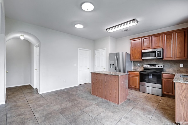 2702 Harvest Crk, San Antonio, TX 78244 - kitchen with stainless steel appliances, a kitchen island, light stone countertops, decorative backsplash, and arched walkways