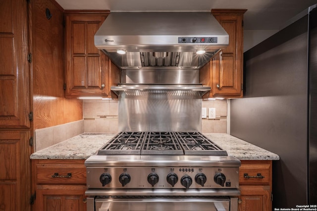 14519 Parksite Woods, San Antonio, TX 78249 - kitchen with appliances with stainless steel finishes, brown cabinetry, backsplash, ventilation hood, and light stone counters