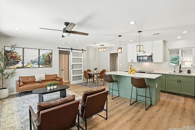 619 Olney Dr, San Antonio, TX 78209 - kitchen featuring green cabinets, stainless steel microwave, a barn door, a kitchen bar, and light wood-style floors