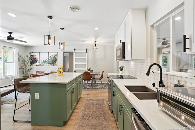 619 Olney Dr, San Antonio, TX 78209 - kitchen featuring green cabinetry, appliances with stainless steel finishes, a barn door, a ceiling fan, and decorative backsplash