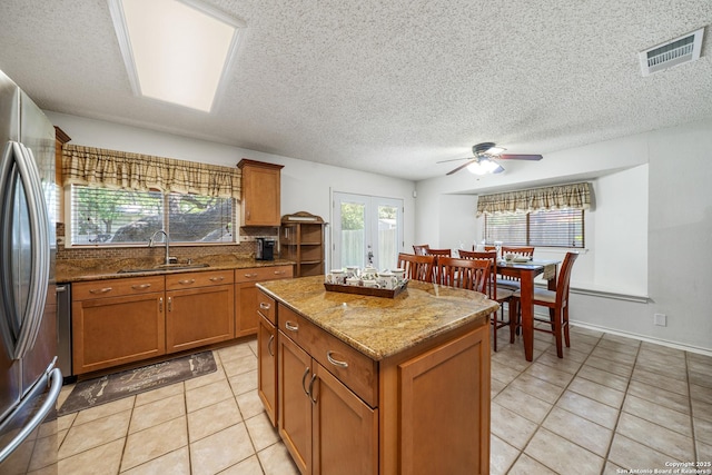 8810 Sebec Cir, San Antonio, TX 78250 - kitchen with stainless steel refrigerator, brown cabinets, ceiling fan, light tile patterned flooring, and a textured ceiling