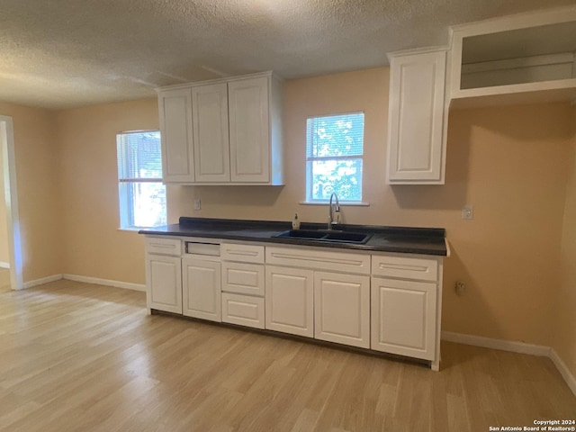 305 Osage, Refugio, TX 78377 - kitchen featuring a textured ceiling, light wood-style floors, white cabinets, and plenty of natural light